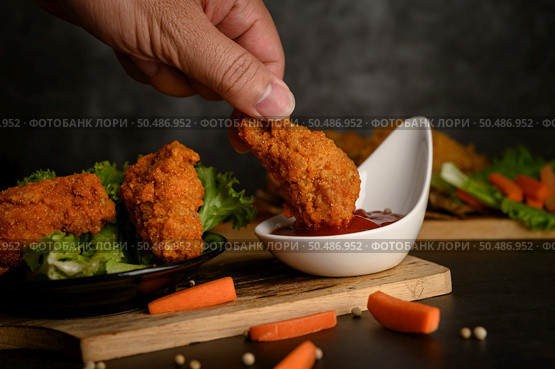 Hand holding crispy fried chicken dipped in tomato sauce. Selective focus. Стоковое фото, агентство Ingram Publishing / Фотобанк Лори