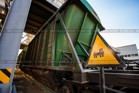 Handmade yellow "Train" road sign. Focus on foreground. Green hopper car on rails blurred on background. Loading and filling terminal of fertilizers plant. Стоковое фото, фотограф Alexey Rezvykh / Фотобанк Лори