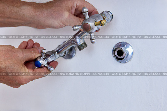 Hands are removing used two handle faucet from wall fitting, worn metal fixture with cross handles and missing spout is separated from exposed connector. Стоковое фото, фотограф Владимир Григорьев / Фотобанк Лори