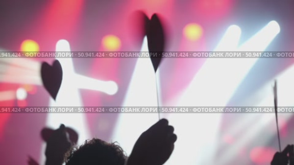 Hands holding heart-shaped signs at a vibrant concert with colorful lights and energetic atmosphere. Стоковое видео, видеограф Данил Руденко / Фотобанк Лори
