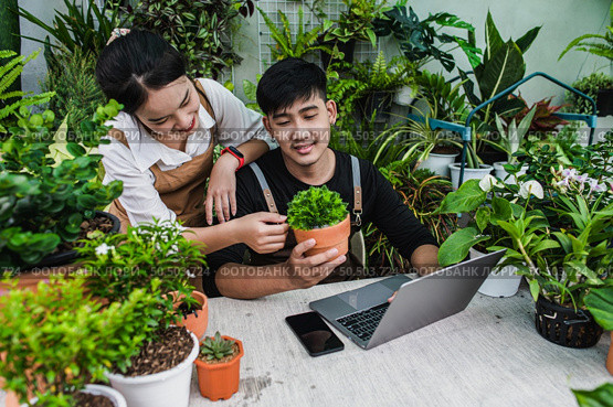 Happily gardener couple use laptop computer while online tutorial on potted plans in workshop together, vlogging or small business houseplant concept. Стоковое фото, агентство Ingram Publishing / Фотобанк Лори