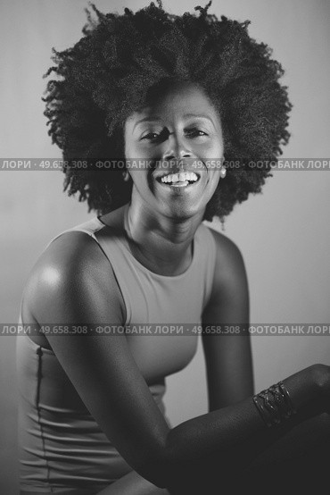 Happy African American woman with curly hair smiling and looking at camera under violet neon light. Black and white photograph.. Black and white photograph of cheerful black model looking at camera. Стоковое фото, агентство Ingram Publishing / Фотобанк Лори
