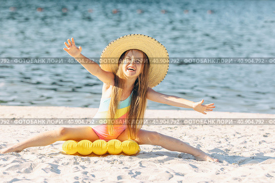 Happy cute smiling little girl in straw hat has fun on the sand on a beach in a swimsuit. Summer concept. Стоковое фото, фотограф Ирина Михайличенко / Фотобанк Лори