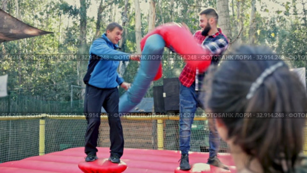 Happy male friends fighting by big stuffed boxing gloves at outdoor amusement playground. Стоковое видео, видеограф Яков Филимонов / Фотобанк Лори