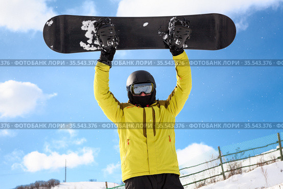 Happy male snowboarder over blue sky in mountains rising up his board. Стоковое фото, фотограф Кекяляйнен Андрей / Фотобанк Лори