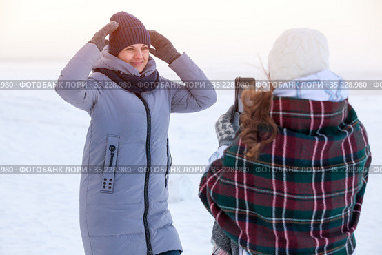 Happy young Caucasian girls taking picture of themselves through cellphone in cold winter seashore. Стоковое фото, фотограф Кекяляйнен Андрей / Фотобанк Лори