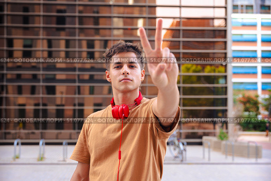 Happy young man raising fist in celebration wearing red headphones outdoors. Стоковое фото, фотограф Raquel Corcoles Mendez / Фотобанк Лори