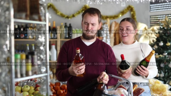 Happy young married couple choosing alcohol in grocery section of supermarket to celebrate Christmas. Стоковое видео, видеограф Яков Филимонов / Фотобанк Лори
