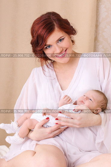 Happy young mother in a white silk dress, holds her baby in her arms and smiling. Стоковое фото, фотограф Светлана Додух / Фотобанк Лори