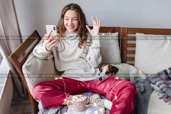 Happy young woman at home indoors sitting on a sofa and talking by videocall. Стоковое фото, фотограф Гладских Татьяна / Фотобанк Лори