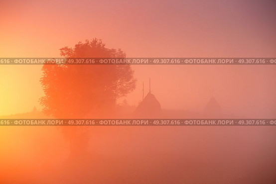 Haystacks and tree in misty autumn morning sunrise. Dawn over mountain fields. Стоковое фото, агентство Ingram Publishing / Фотобанк Лори