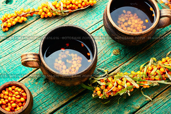 Healing tea with sea buckthorn on wooden surface. Delicious fresh tea from autumn berries.. Tea with sea buckthorn berries. Стоковое фото, агентство Ingram Publishing / Фотобанк Лори