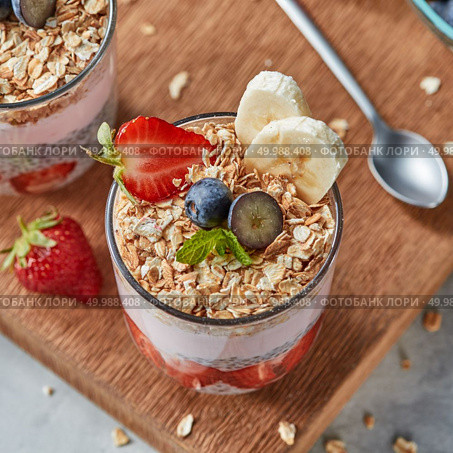 Healthy breakfast with homemde granola, yogurt, slices of strawberries, banana, blueberries, oat flaks, chia seeds on a wooden board. Concept of healthy dieting food.. The glass with oat flakes, banana fruits, strawberries, fresh smoothie, chia seeds on a wooden board. Стоковое фото, агентство Ingram Publishing / Фотобанк Лори
