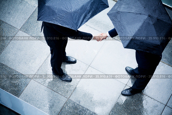 High angle view of two businessmen holding umbrellas and shaking hands in the rain. Стоковое фото, агентство Ingram Publishing / Фотобанк Лори