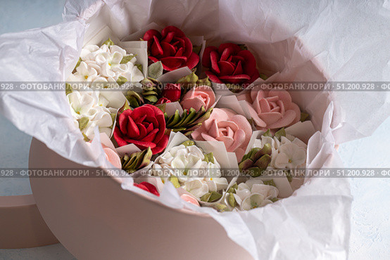 Home-made zephyr floristry arrangement featuring delicate pink, red, and white flowers nestled in soft tissue paper, creating a charming and inviting floral display concept. Стоковое фото, фотограф Ирина Ручушкина / Фотобанк Лори