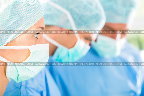Hospital - surgery team in the operating room or Op of a clinic operating on a patient, perhaps it’s an emergency a assistant holding a cotton swap forceps. Surgeons operating patient in operation theater. Стоковое фото, агентство Ingram Publishing / Фотобанк Лори