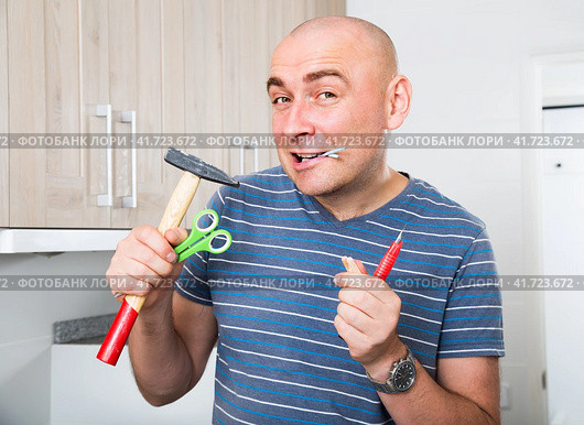 Imposing man holds in teeth of screws and holding hammer. Стоковое фото, фотограф Татьяна Яцевич / Фотобанк Лори