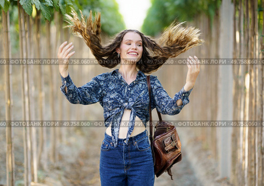 In a picturesque vineyard, a cheerful young woman playfully flips her hair, highlighting her stylish outfit while surrounded by vibrant and lush greenery that adds to the beauty of the scene. A Joyful Young Woman with Flowing Hair Strolling Along a Picturesque Path in a Vineyard. Стоковое фото, агентство Ingram Publishing / Фотобанк Лори
