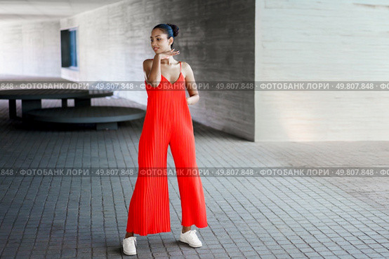 In an urban environment, a stylish and fashionable woman is striking a confident pose while wearing a vibrant red jumpsuit, effectively showcasing her contemporary sense of style and natural grace. A Stylish Woman Dressed in a Bright Red Jumpsuit Gracefully Posing Outdoors in Daylight. Стоковое фото, агентство Ingram Publishing / Фотобанк Лори