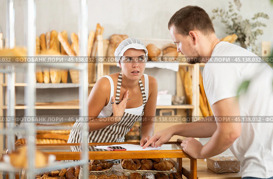 In bakery, male visitor and female salesperson work with paper documents and count using phone. Стоковое фото, фотограф Яков Филимонов / Фотобанк Лори