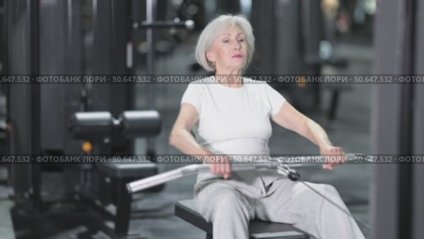 In gym, senior woman uses cable row machine to strengthen arm muscles. Стоковое видео, видеограф Яков Филимонов / Фотобанк Лори