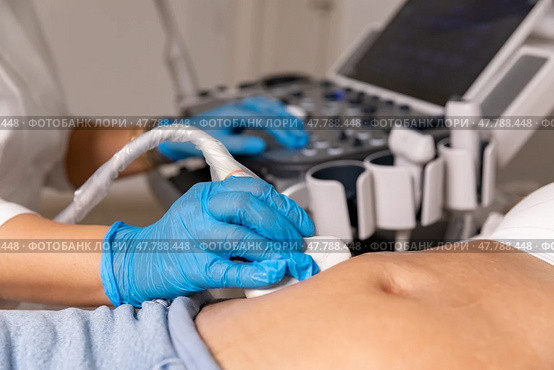 In the hospital, close-up shot of the doctor does ultrasound sonogram procedure to a pregnant woman. Obstetrician moving transducer on the belly of the future mother. High quality photo. Стоковое фото, фотограф Ирина Михайличенко / Фотобанк Лори