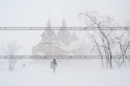 In winter, during a blizzard near the Cathedral of the Holy Trinity. People go through a snowstorm.Anadyr city, Chukotka, Russia. Стоковое фото, фотограф Андрей Степанов / Фотобанк Лори