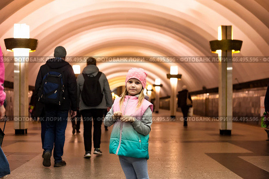 Inside the subway, a cheerful five-year-old girl stands out against the backdrop of busy commuters. Dressed warmly, she radiates joy amid the hustle of the underground. Стоковое фото, фотограф Aleksandr Golubev / Фотобанк Лори