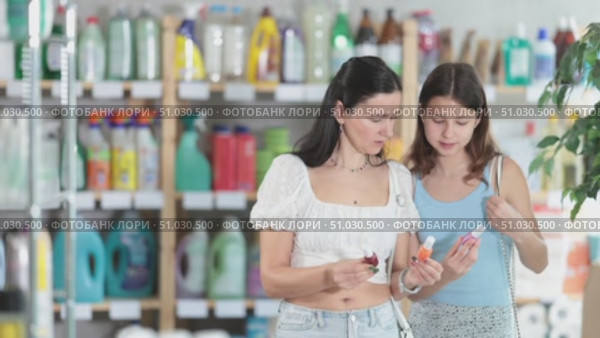 Interested preteen girl with mom in casual summer outfits examining small bottles of brightly colored nail polish during shopping in beauty section of supermarket. Стоковое видео, видеограф Яков Филимонов / Фотобанк Лори