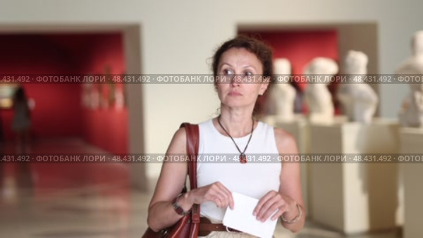 Interested woman looking closely at classical statues in museum and holding tour sheet in hands. Стоковое видео, видеограф Яков Филимонов / Фотобанк Лори
