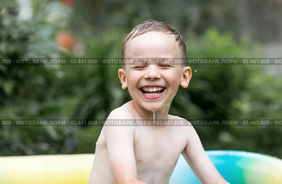 It's a hot day. A cute boy is swimming and splashing in the pool. A happy little boy smiles at the camera. Splashes of water are flying in all directions. The concept of summer holidays with children. Стоковое фото, фотограф Photojuli / Фотобанк Лори