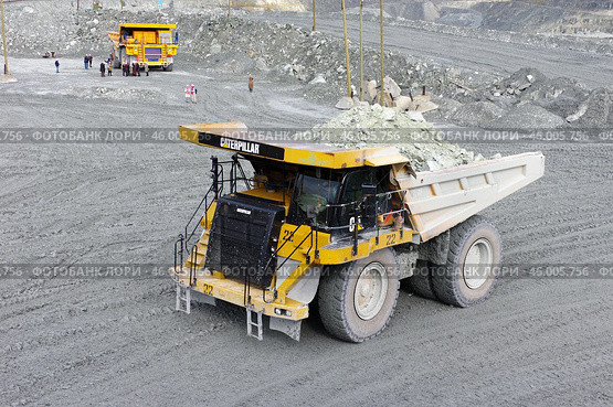 Карьерный самосвал "Caterpillar" на переднем плане, карьерный самосвал "БелАЗ" на заднем плане, экскурсанты рассматривают пейзажи. Карьер комбината "Ураласбест" (2019 год). Редакционное фото, фотограф Алексей Иванов / Фотобанк Лори
