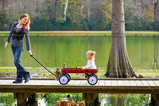 Kid girl and mother walking in the park lake with pull cart. Стоковое фото, агентство Ingram Publishing / Фотобанк Лори