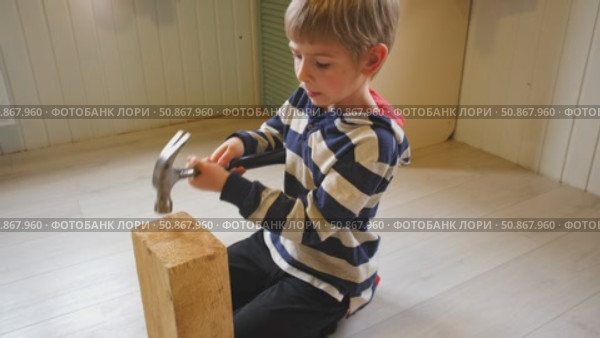 Kid hammers nails to wood with a hammer. Little boy helping with toy tools. Funny 6 years child having fun on building. Kid hammering crafting stuff using wooden pieces. Carpentry and family concept. Стоковое видео, видеограф Марина Демидюк / Фотобанк Лори