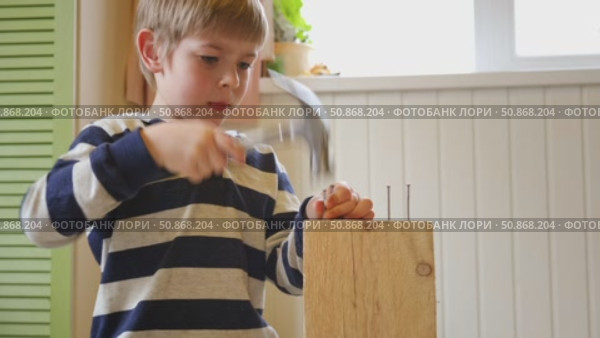 Kid hammers nails to wood with a hammer. Little boy helping with toy tools. Funny 6 years child having fun on building. Kid hammering crafting stuff using wooden pieces. Carpentry and family concept. Стоковое видео, видеограф Марина Демидюк / Фотобанк Лори
