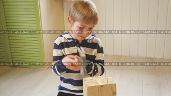 Kid hammers nails to wood with a hammer. Little boy helping with toy tools. Funny 6 years child having fun on building. Kid hammering crafting stuff using wooden pieces. Carpentry and family concept. Стоковое видео, видеограф Марина Демидюк / Фотобанк Лори