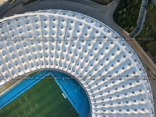 KIEV, UKRAINE - July 19, 2018. Panoramic view from drone of the National Sports Complex Olimpiysky at summer sunset - the stadium cover structure. Abstract architecture photo. Construction of the stadium roof, firld and tribunes.. KYIV, UKRAINE - July 19, 2018. NSC Olimpiysky the birds eye view from drone of construction the stadium roof, green football field, tribunes of complex. Редакционное фото, агентство Ingram Publishing / Фотобанк Лори