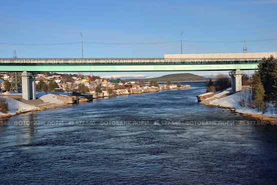 Knyazhaya Guba Village, urban settlement of Zelenoborsky, Kandalaksha district, Murmansk region, March 23, 2024: Automobile bridge across Knyazhegubskaya hydroelectric power station canal at confluence in Knyazhaya Guba of White Sea. Редакционное фото, фотограф Алексей Антипов / Фотобанк Лори