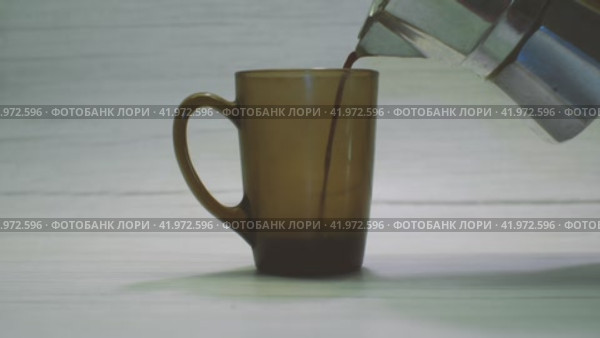 Кофе наливается из гейзерной кофеварки в кружку из черного стекла на светлом фоне. Процесс приготовления вкусного кофе в домашних условиях. Стоковое видео, видеограф Воловодов Владимир / Фотобанк Лори