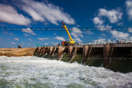Kok-aral, Kazakhstan - May 03, 2012: Aral Sea Kok-aral dam. Water discharge in flood. Open shutters. Yellow mobile crane and workers on dam. Стоковое фото, фотограф Alexey Rezvykh / Фотобанк Лори