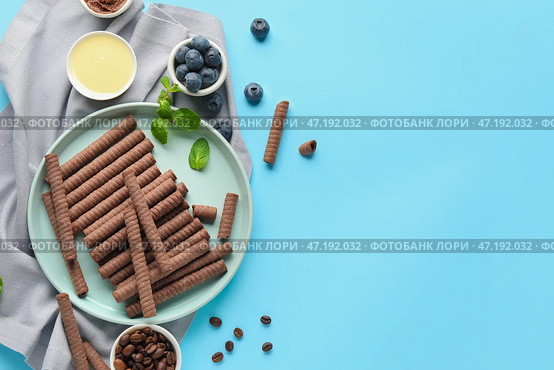 Композиция с вкусными шоколадными вафельными трубочками, черникой, кофейными зернами, сгущенным молоком и мятой на синем фоне. Стоковое фото, фотограф Pixel_shot / Фотобанк Лори