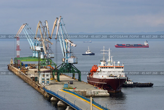 Корсаковский морской торговый порт, Город Корсаков, Сахалинская область, Дальний Восток России. Вид на морпорт. Около причала пришвартовано пассажирское судно. На пирсе портовые краны. Вдали на рейде грузовые суда и буксировщики. Морская транспортная инфраструктура Сахалина. Залив Анива, Охотское море. Стоковое фото, фотограф Андрей Степанов / Фотобанк Лори