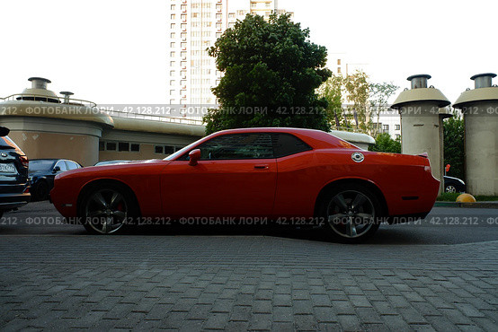 Красный гоночный автомобиль Додж Челленджер СРТ на парковке. Red Dodge Challenger SRT in the parking, side view. Summer sunset view. (2021 год). Редакционное фото, фотограф Александр Кузнецов / Фотобанк Лори