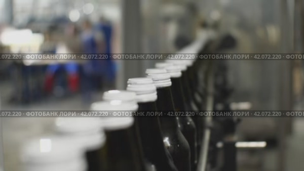 Крупным планом стеклянные бутылки с водой на конвейере Акцент на белых крышках. Цех по производству минеральной воды и безалкогольных напитков. Стоковое видео, видеограф Воловодов Владимир / Фотобанк Лори
