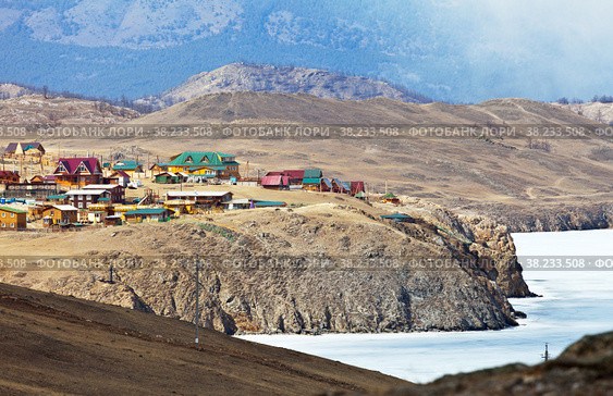 Lake Baikal in early spring. Top view of the village of Sakhyurta and the wooden houses of tourist bases on the coastal rocks. Snowless hills on the shore of Tutai Bay with melting ice. Spring travel (2015 год). Стоковое фото, фотограф Виктория Катьянова / Фотобанк Лори