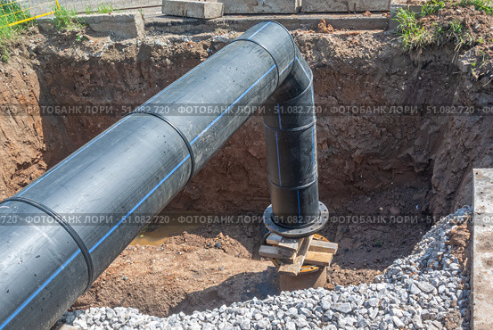 Large diameter plastic pipe for water supply. A smooth black plastic pipe with a blue stripe is placed in the trench. Installation of water supply systems. The excavation where the pipes are connected. Стоковое фото, фотограф Эдуард Белкин / Фотобанк Лори