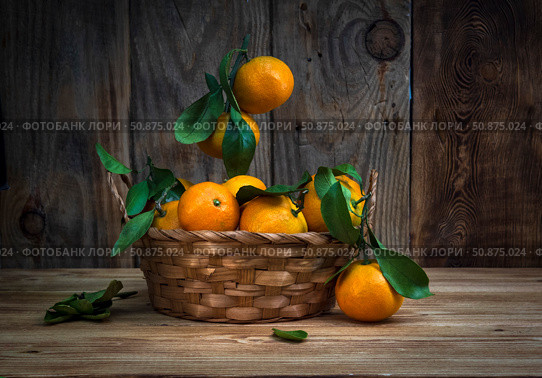 Large ripe tangerines with green leaves lie in a wicker basket on a wooden tabletop. Selective focus. Стоковое фото, фотограф Анищенко Геннадий / Фотобанк Лори