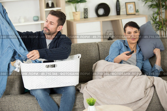 lazy woman with remote watching tv with man doing laundry. Стоковое фото, агентство Ingram Publishing / Фотобанк Лори
