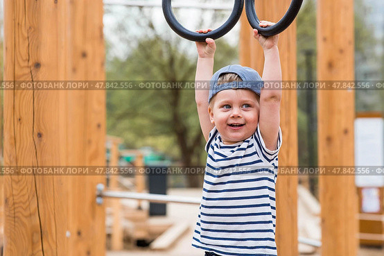 Lifestyle. A cute little boy is hanging on rings on a sports field in the fresh air. The concept of children's sports and physical development. Стоковое фото, фотограф Photojuli / Фотобанк Лори