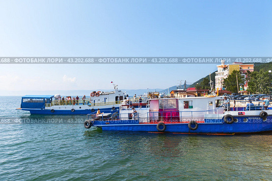 LISTVYANKA VILLAGE, IRKUTSK REGION, RUSSIA - August 03, 2023: View of Baikal Lake embankment in village of Listvyanka, pleasure boats and popular Mayak hotel on sunny summer day. Редакционное фото, фотограф Виктория Катьянова / Фотобанк Лори